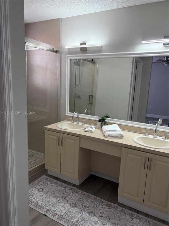 Dual-sink vanity with solid-surface countertop, full-width mirror, inset cabinetry, and glass-enclosed shower