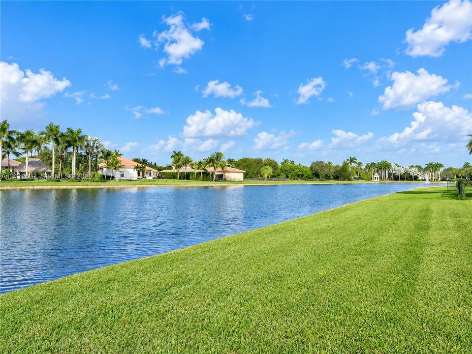 Waterfront lot featuring a large body of water, expansive manicured lawn, and mature palm trees