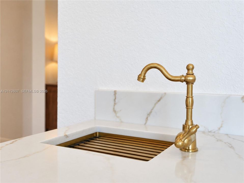 Integrated stone-finish countertop with a coordinating backsplash, featuring a custom metal-finish sink basin and a decorative brass-finish gooseneck faucet