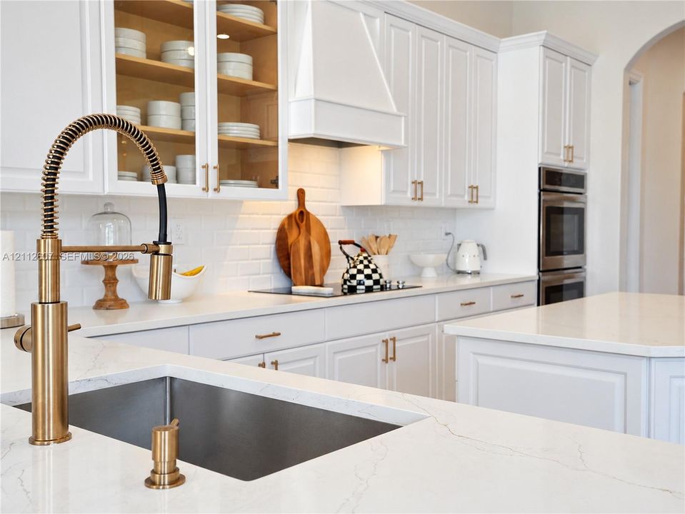 Kitchen featuring white cabinetry with gold-tone hardware, stone countertops, a subway tile backsplash, a high-arc professional style faucet, and built-in double wall ovens