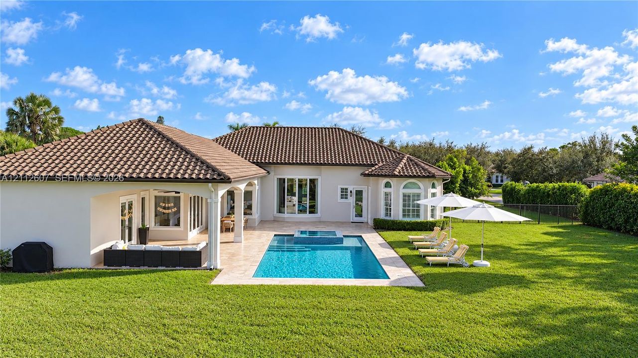 Exterior featuring a tiled roof, covered patio, swimming pool with integrated spa, paved pool deck, and expansive lawn
