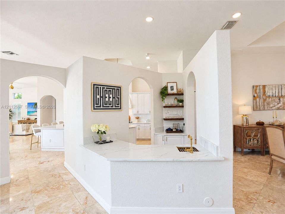 Custom wet bar featuring a stone-look countertop, brass-finish faucet, built-in cabinetry, arched entryways, and stone-finish flooring