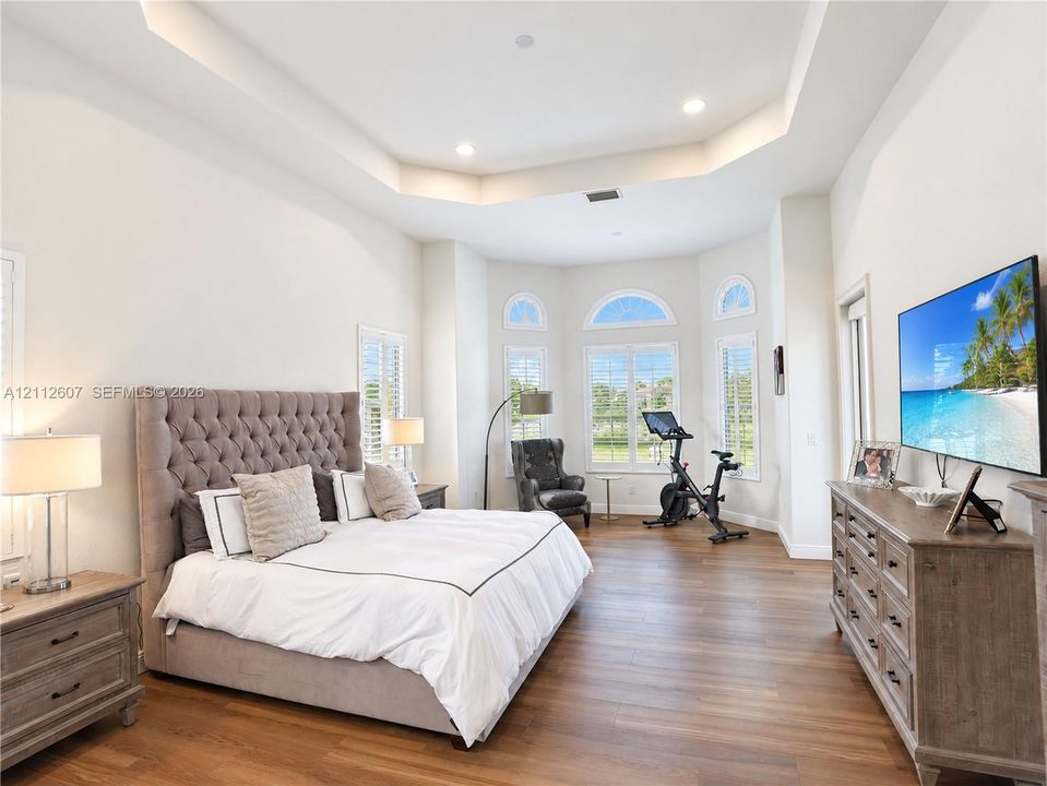 Tray ceiling with recessed lighting, wood-finish flooring, and expansive bay windows featuring arched transoms and plantation shutters