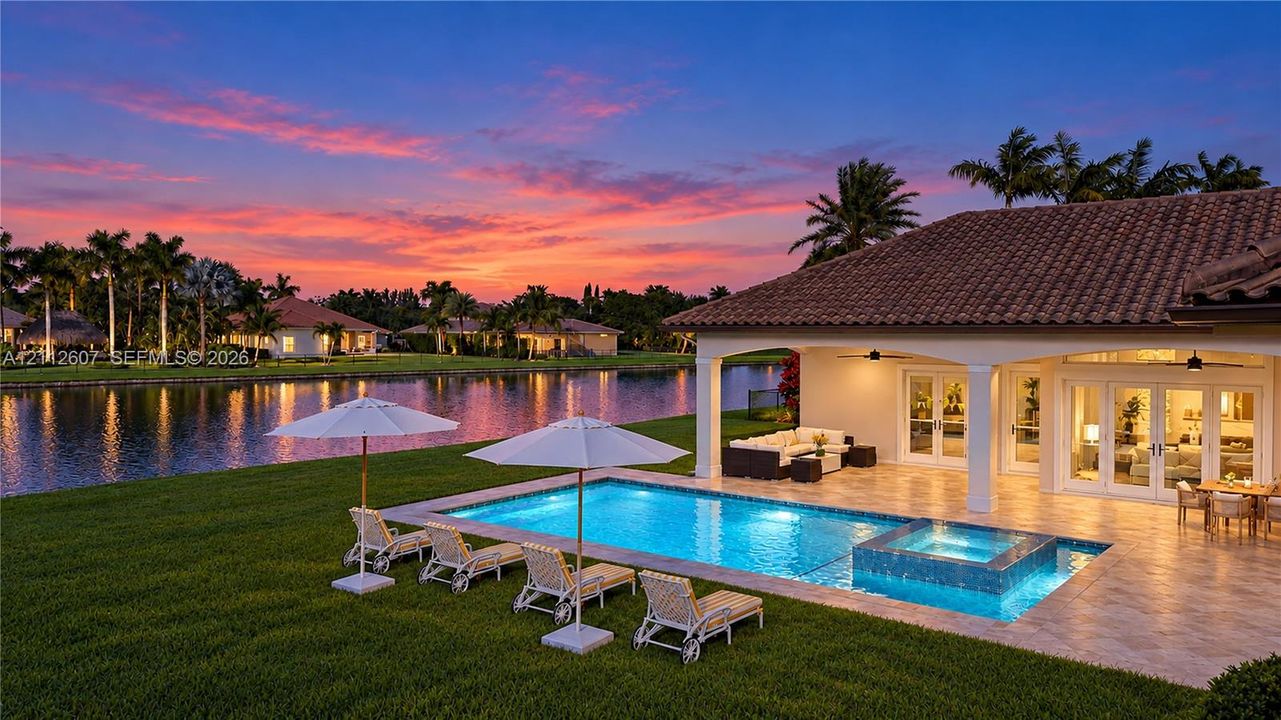 Waterfront outdoor space featuring a covered tile patio, a built-in swimming pool with a raised spa, and manicured landscaping