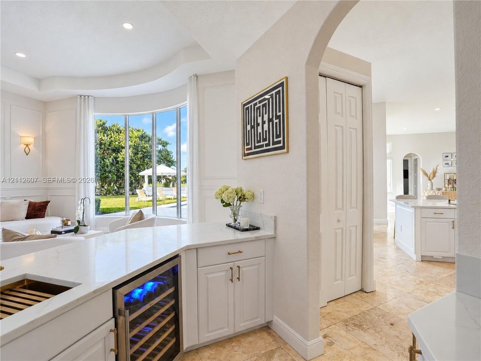 Kitchen area featuring quartz countertops, a built-in wine refrigerator, paneled cabinetry, stone flooring, and an arched entryway