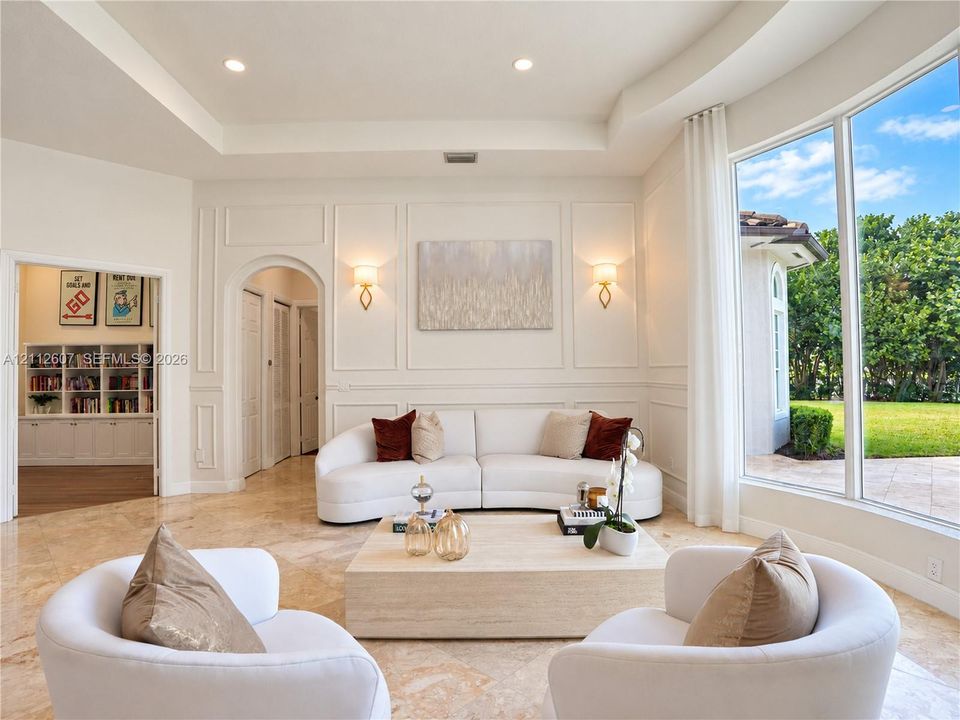 Living area featuring tray ceilings, wainscoting, arched architectural details, polished stone flooring, and expansive floor-to-ceiling windows