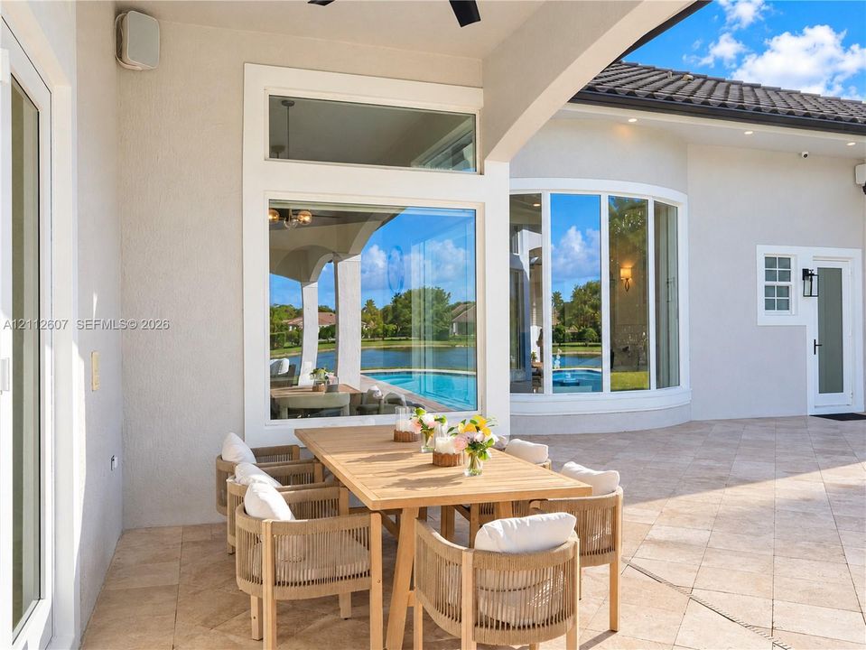 Covered lanai featuring neutral stone tile flooring, an integrated ceiling fan, expansive glass picture windows, and a curved architectural wall detail