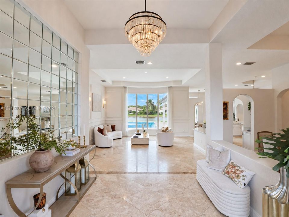 Foyer featuring large-scale polished stone flooring, a multi-tiered crystal chandelier, and a floor-to-ceiling grid-patterned wall mirror