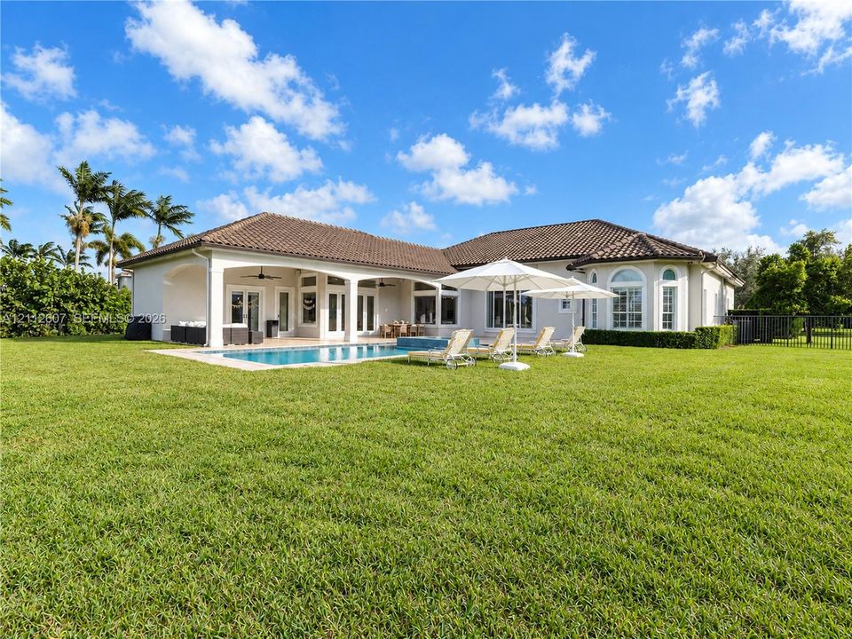 Exterior featuring a tile roof, covered patio with arched supports, built-in swimming pool with masonry deck, and expansive lawn
