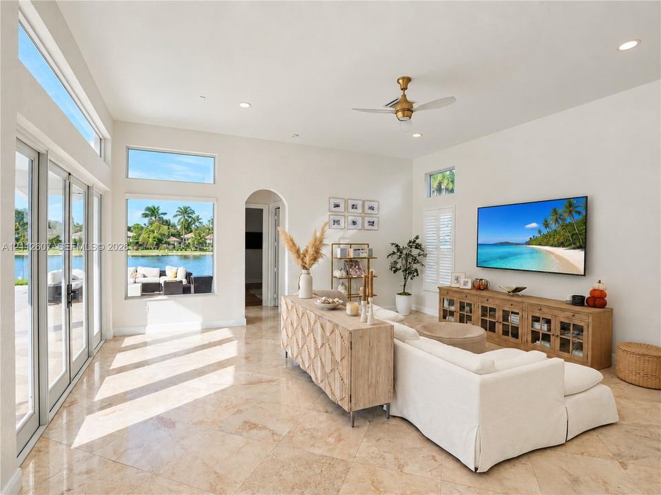 Living area featuring expansive windows, natural stone flooring, high ceilings, an arched doorway, and a brushed gold ceiling fan