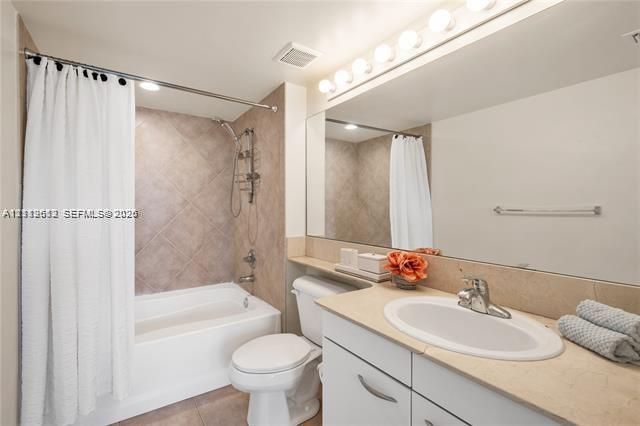 Bathroom featuring a recessed tub with a tile surround, a built-in vanity with a solid-surface countertop, an integrated oval sink, and a full-width wall mirror with an integrated light fixture