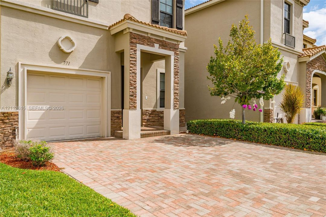 Stucco exterior featuring stacked-stone accents, paver driveway, covered entryway, and attached garage