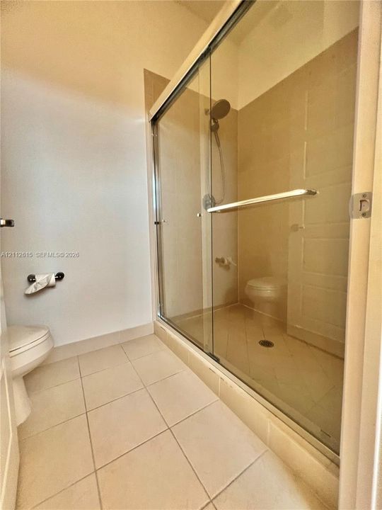 Shower featuring a sliding glass enclosure, tile surround, and adjustable handheld shower head, complemented by tile flooring and a dual-flush toilet