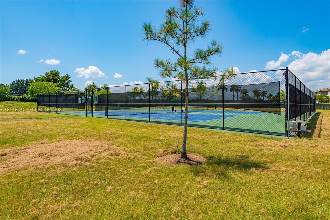 Enclosed tennis court featuring a hard surface, perimeter chain-link fencing, and dark mesh screening