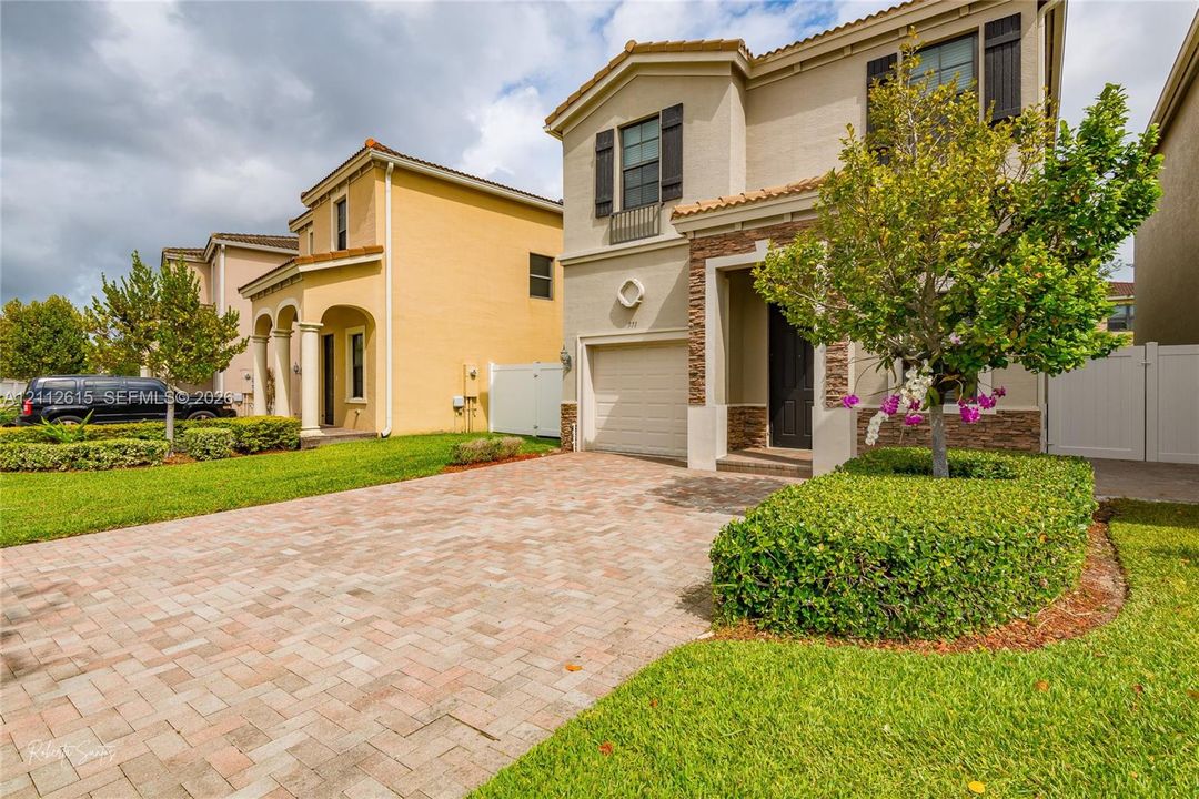 Two-story exterior featuring a paver driveway, stone veneer accents, multi-pane windows with dark shutters, and a tile roof