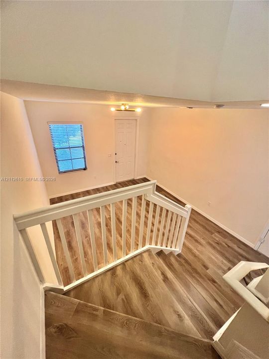 Vaulted ceilings, wood-finish flooring, white wooden stair railings, and a multi-pane window