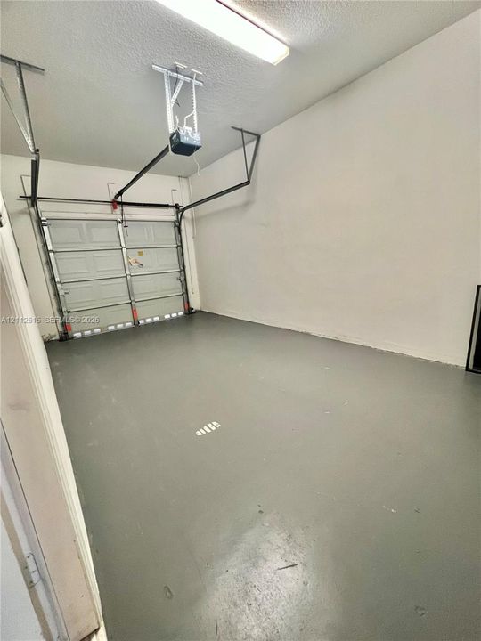 Finished garage interior featuring a smooth-finish floor, white walls, and a mounted overhead garage door operator with integrated lighting