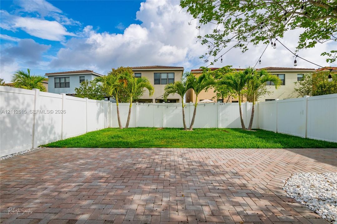 Backyard featuring a paver patio, a manicured lawn, perimeter vinyl fencing, and palm trees