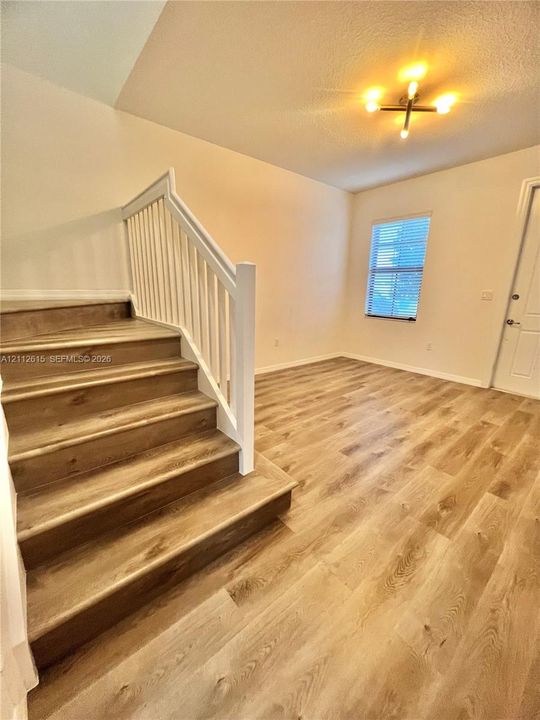 Interior space featuring wood-finish flooring, a wooden staircase with a white railing, a multi-arm flush-mount light fixture, and a single-hung window