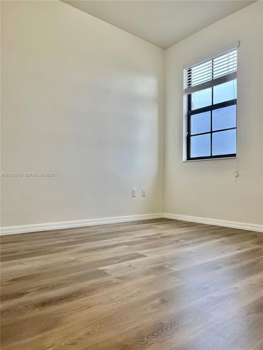 Neutral-toned walls, wood-finish flooring, and a multi-pane window featuring horizontal blinds