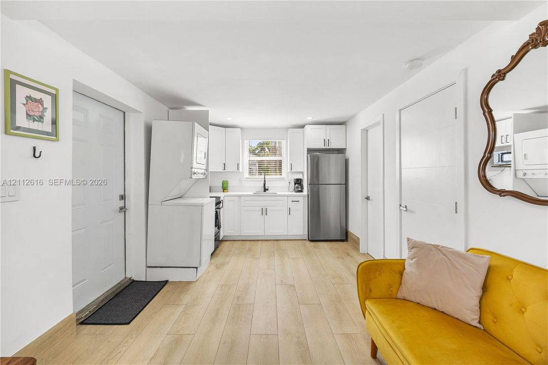Kitchen featuring white cabinetry, wood-finish flooring, a stainless steel refrigerator, and a stacked laundry unit
