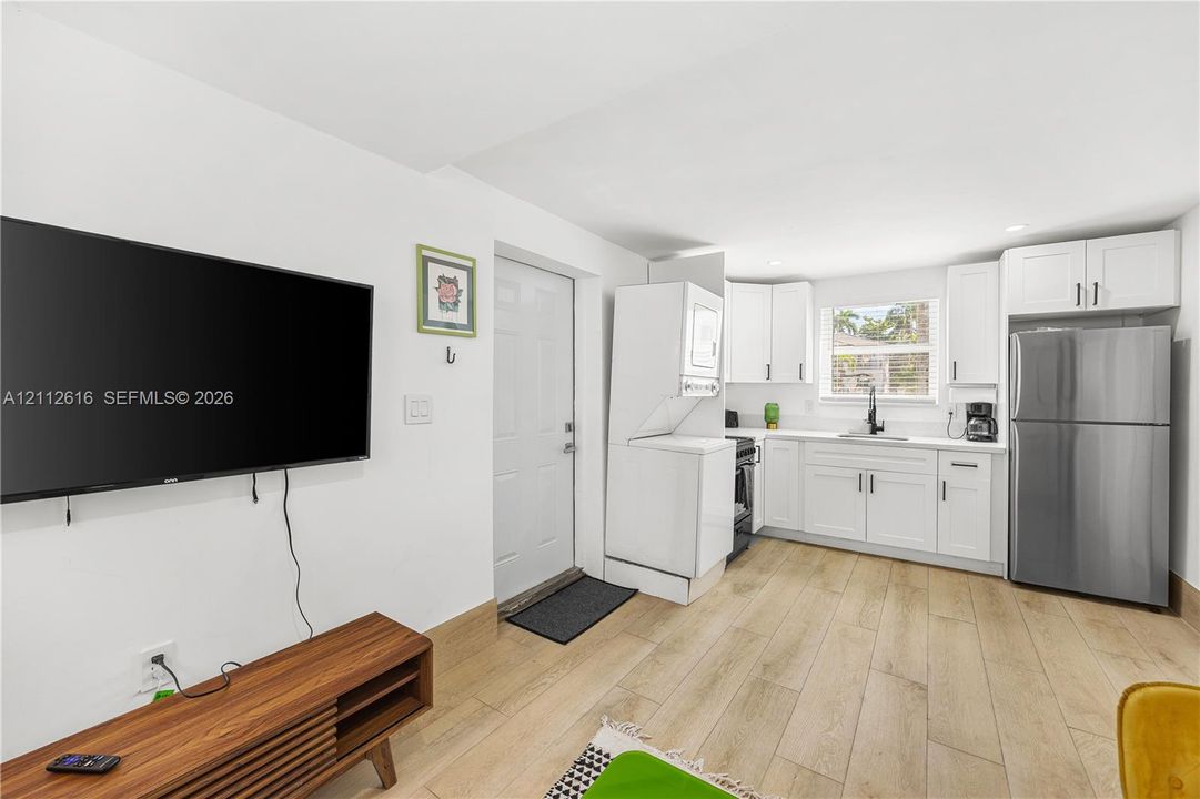 Kitchenette featuring white cabinetry, wood-finish flooring, stainless steel refrigerator, and integrated laundry unit