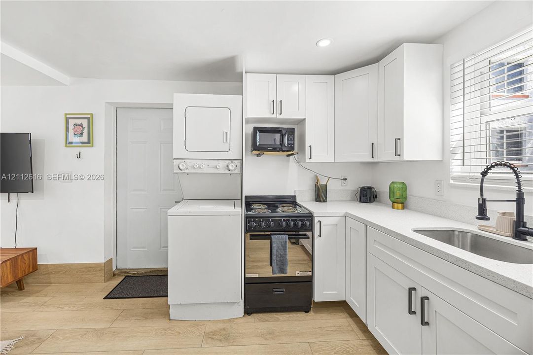 Kitchen featuring white cabinetry, solid-surface countertops, a stainless steel sink with a matte black faucet, a built-in laundry center, and wood-finish flooring