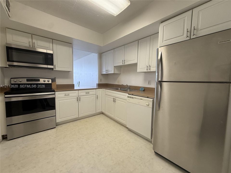 Kitchen featuring white shaker-style cabinetry, solid-surface countertops, stainless steel appliances, and built-in lighting
