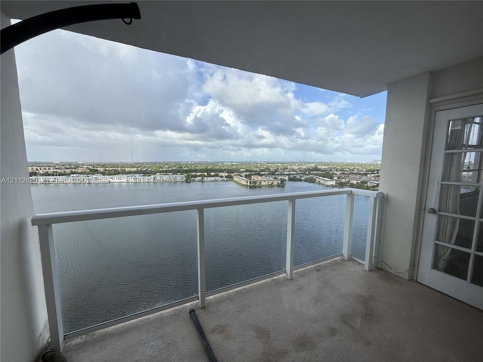 Covered balcony featuring a white railing and a door with glass panes, overlooking an expansive water expanse and horizon