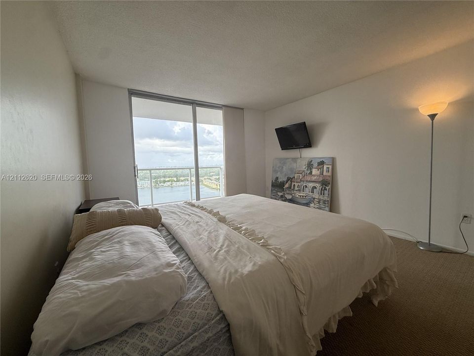 Floor-to-ceiling sliding glass door providing natural light and exterior water scenery, accompanied by a private balcony with a metal railing