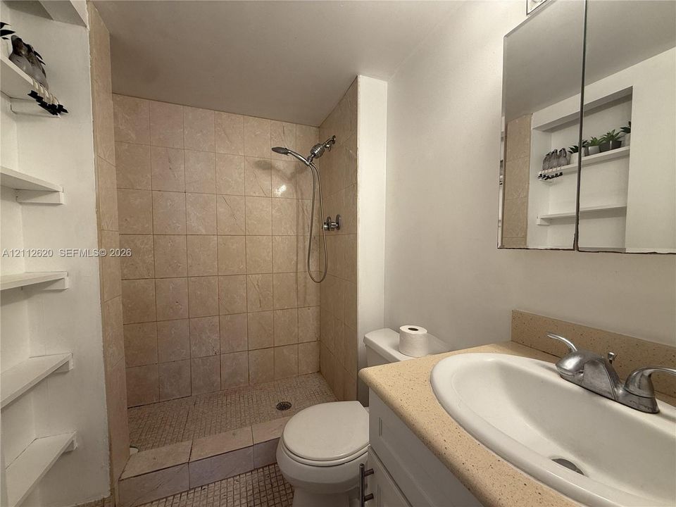 Bathroom featuring a walk-in shower with tile surround, built-in recessed shelving, vanity with a solid surface countertop, integrated sink basin, and a mirrored medicine cabinet