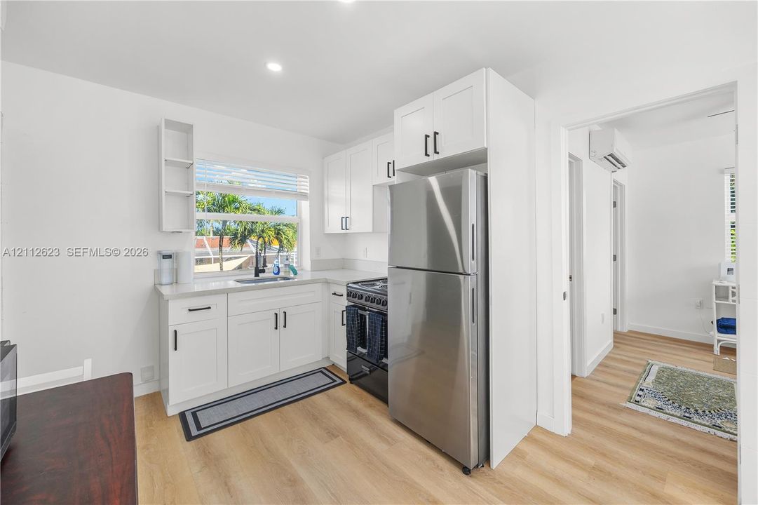 Kitchen featuring white cabinetry with black hardware, stainless steel refrigerator, dark range, light-toned wood-finish flooring, and quartz countertops