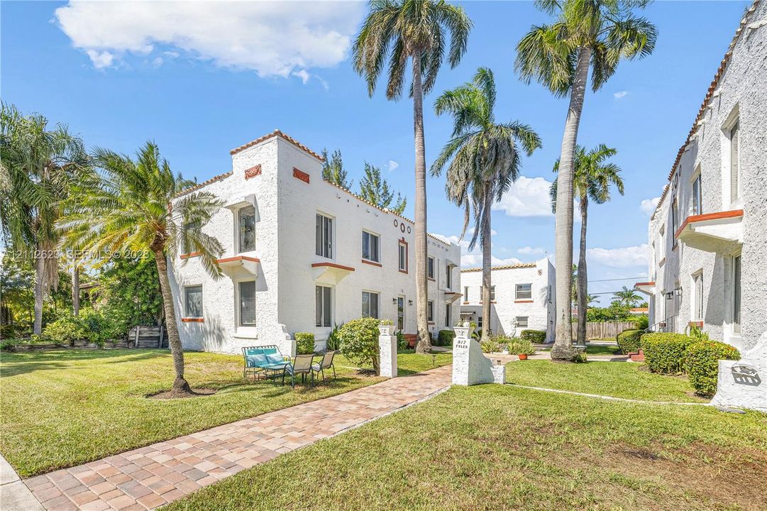 Mediterranean-style architecture featuring textured white stucco exterior, clay-tile roof accents, decorative architectural molding, paver walkway, and mature palm trees