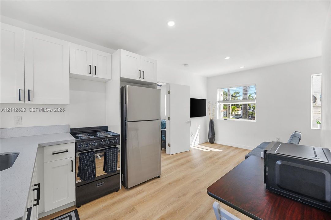Kitchen featuring white shaker-style cabinetry, stainless steel appliances, light-toned solid surface countertops, and wood-finish flooring