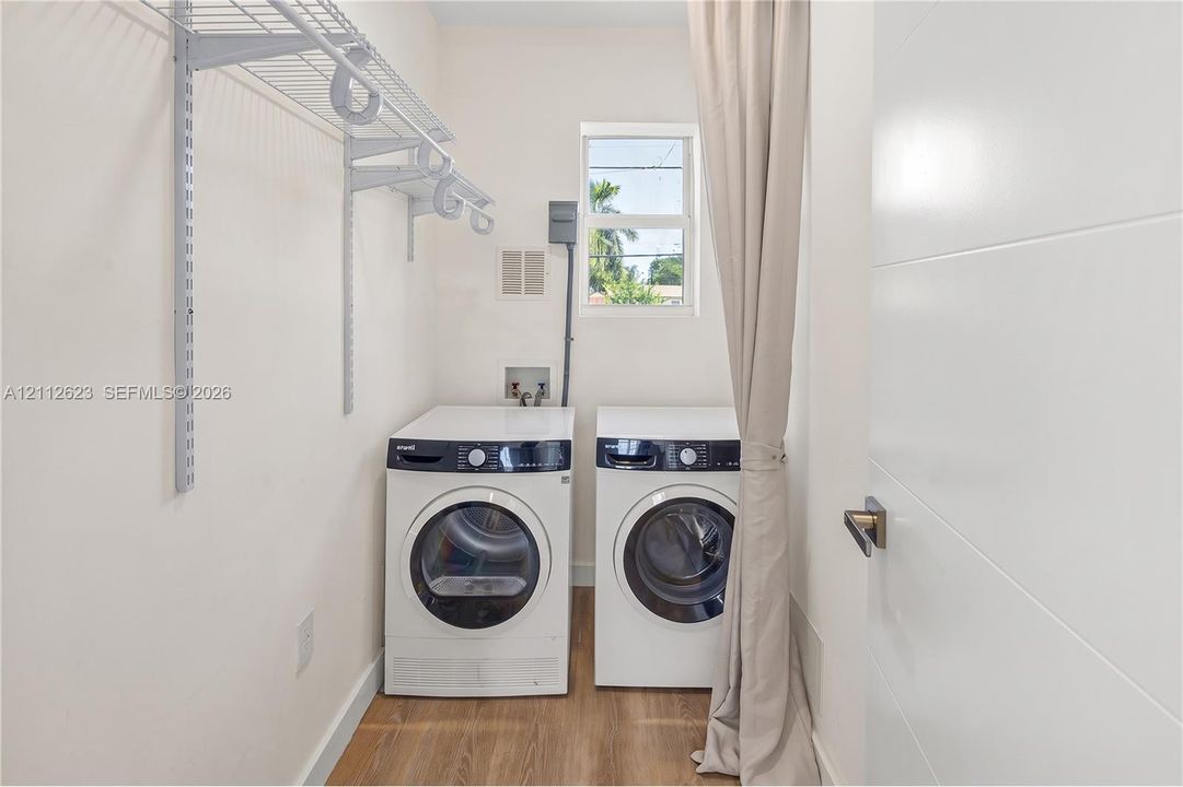 Laundry area featuring wood-finish flooring, white walls, and built-in white wire shelving