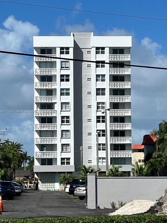 Multi-story residential building featuring a white facade, symmetrical balconies with decorative railings, and ground-level patterned concrete block screening