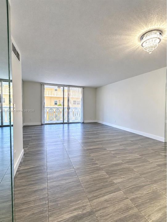 Open floor plan featuring wood-finish tile flooring, a crystal flush-mount light fixture, a floor-to-ceiling mirrored wall, and glass sliding doors providing access to a balcony