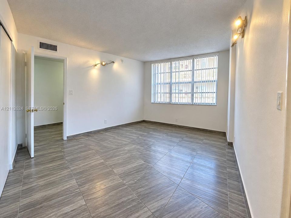 Interior room featuring large-format wood-finish tile flooring, vertical blinds over a multi-pane window, and wall-mounted light fixtures