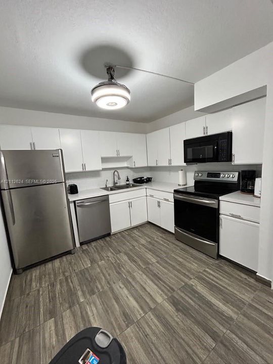 Kitchen featuring white cabinetry, solid-surface countertops, stainless steel appliances, and wood-finish flooring