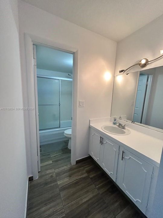 Bathroom featuring a white vanity with an integrated countertop, oval basin, expansive wall-mounted mirror, brushed-finish light fixture, and wood-finish tile flooring