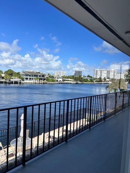 Covered balcony featuring black metal railings, smooth surface flooring, and water frontage
