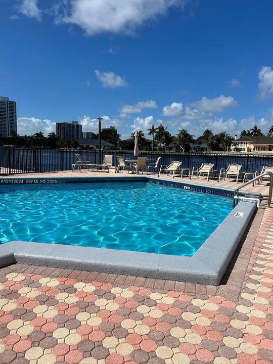 In-ground pool with concrete coping, decorative paver decking, and a metal perimeter fence overlooking the waterway
