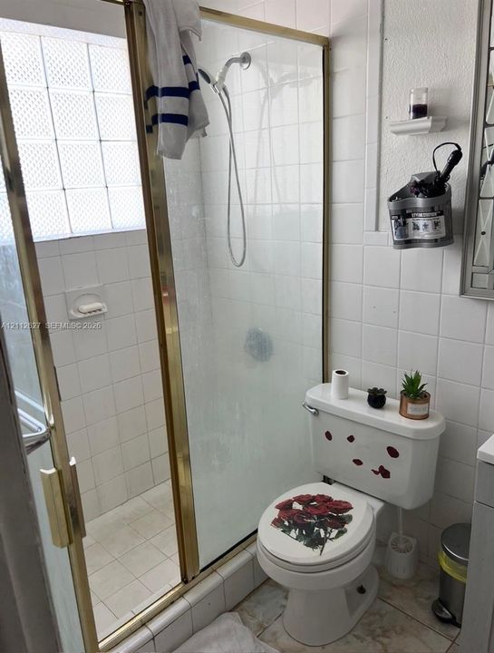 Walk-in shower enclosure featuring gold-tone metal framing and integrated glass block window