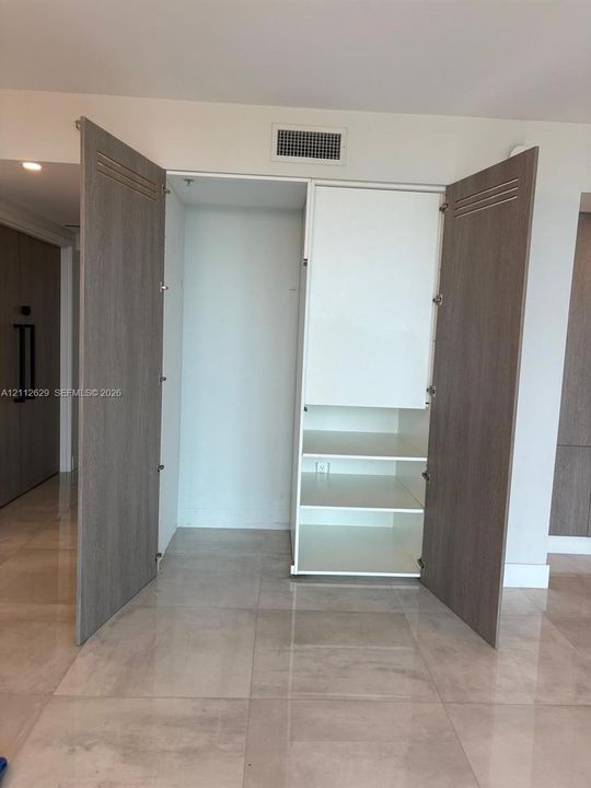 Built-in storage cabinet featuring wood-finish panel doors with horizontal slat detailing, internal shelving, and large-format tile flooring
