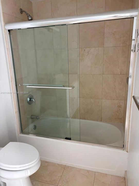 Bathtub and shower combination featuring a glass sliding enclosure, metallic hardware, and neutral-toned wall tile
