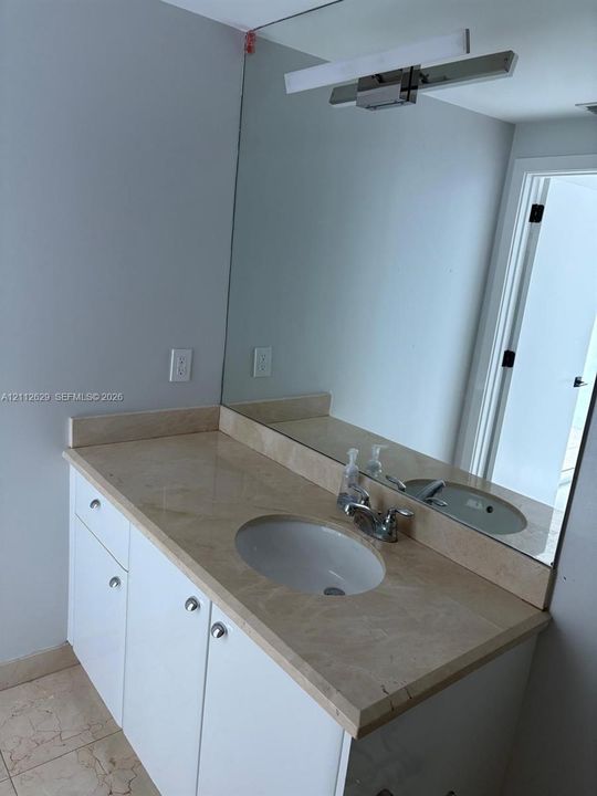 Vanity with a solid surface countertop, integrated oval basin, white cabinetry with round hardware, and a large wall-mounted mirror featuring a linear light fixture