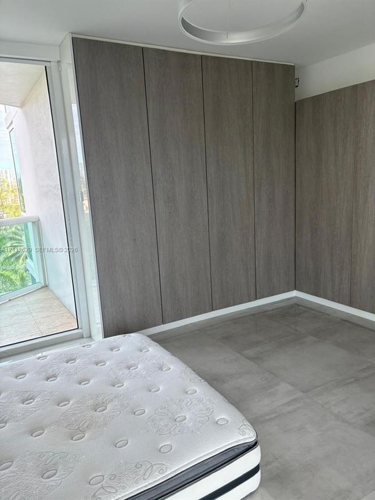 Floor-to-ceiling built-in cabinetry with wood-finish paneling, large-format grey tile flooring, and a sliding glass door opening to a private balcony