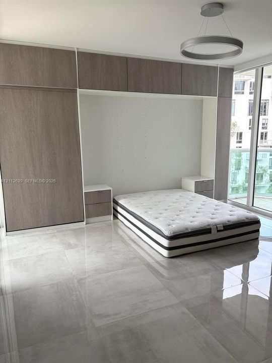 Floor-to-ceiling custom wood-finish cabinetry, built-in dual nightstands, polished large-format tile flooring, modern circular pendant lighting, and floor-to-ceiling glass sliding doors