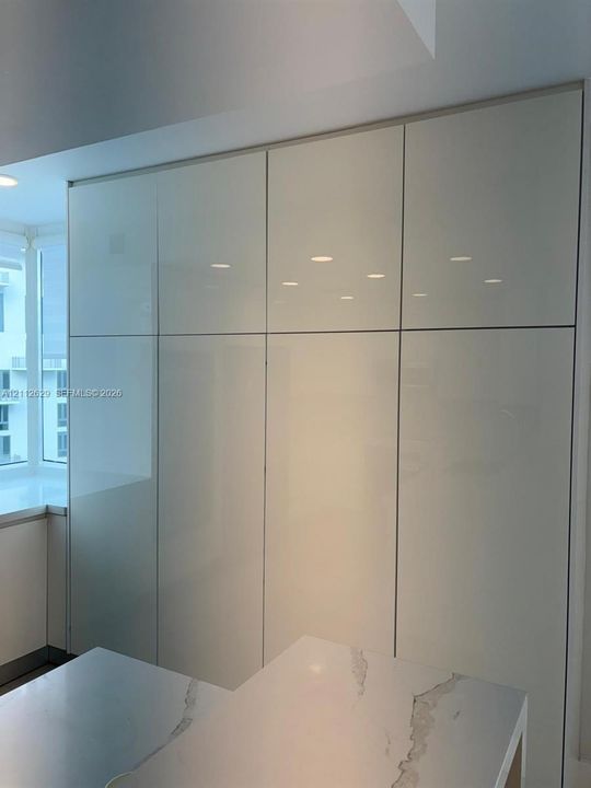 Full-height cabinetry featuring high-gloss, flat-panel doors with integrated hardware and a stone-surface countertop with visible veining