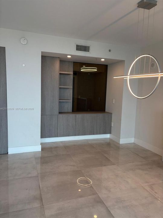 Built-in wood-finish cabinetry featuring open shelving, large-format tile flooring, and a contemporary circular pendant light fixture